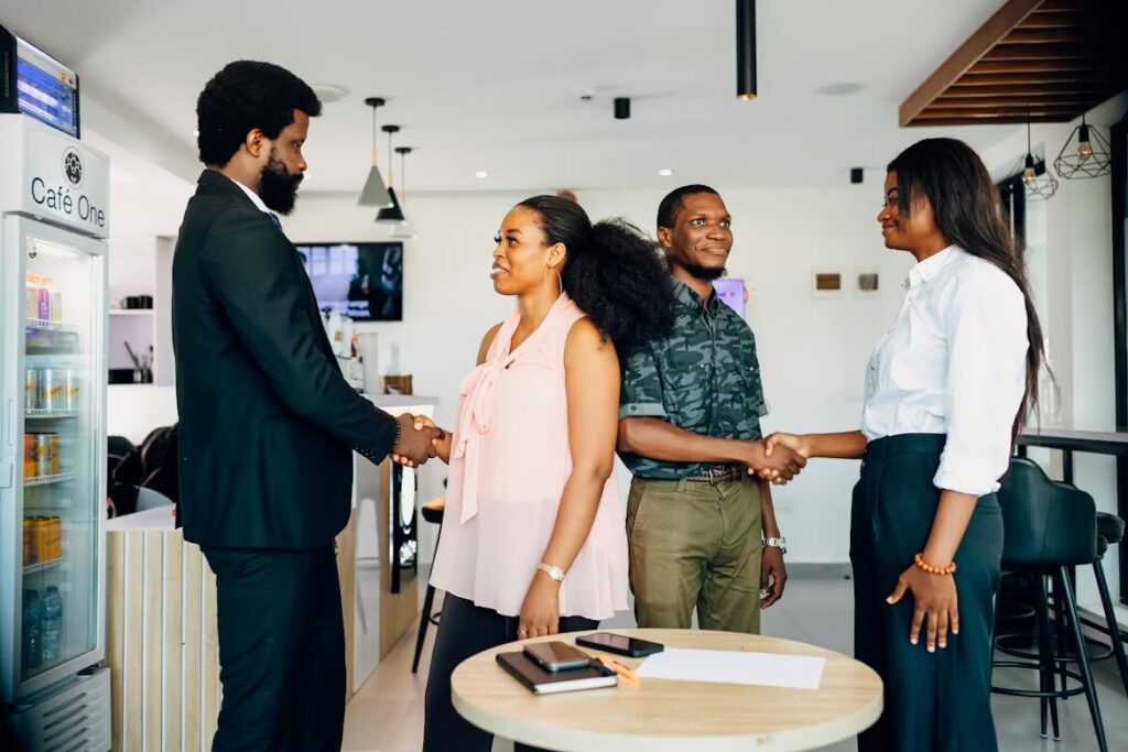 God is Love: A group of four business people are standing around a table shaking hands and talking, portraying human approval